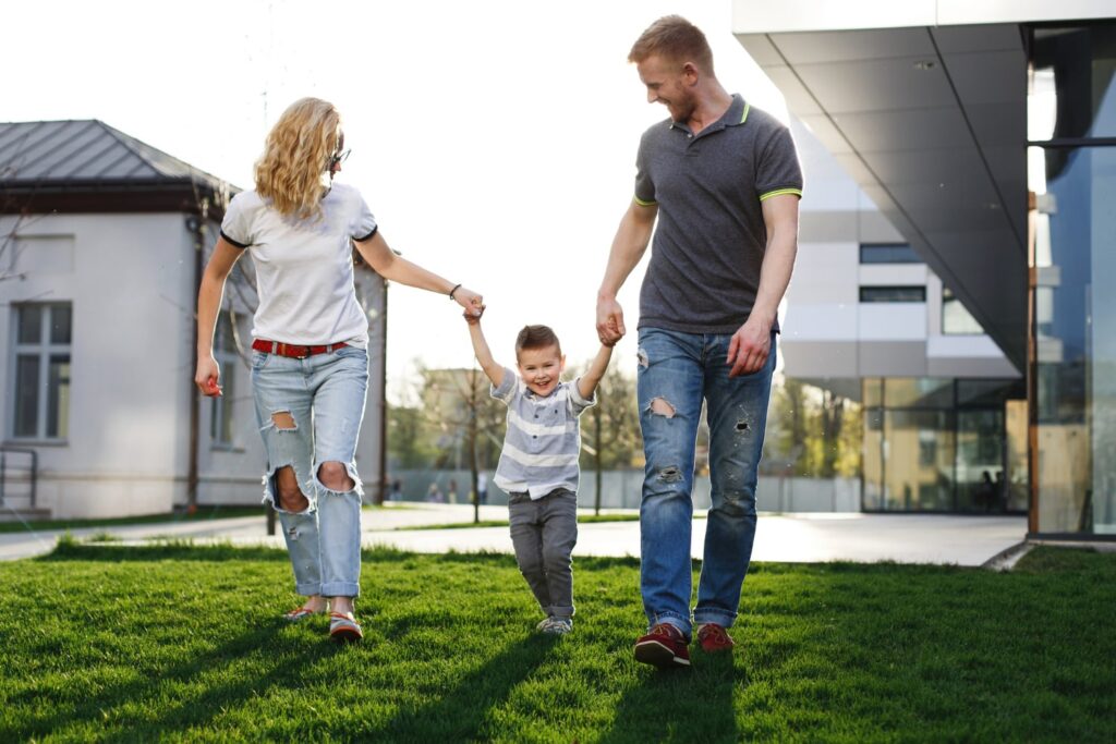 Smiling family walking hand in hand on a green lawn near modern residential buildings, symbolizing lifestyle appeal of buying property in Larnaca.